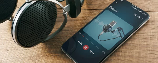 Ein Smartphone liegt auf einem Holztisch und spielt einen Podcast ab, daneben ein Paar Kopfhörer.