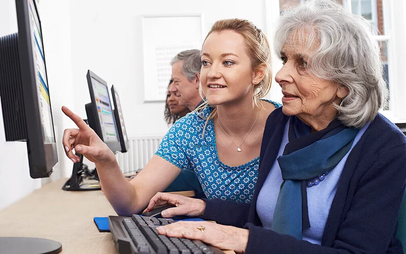 Lebenslanges Lernen: Eine ältere Frau sitzt in einem Computer-Kurs und bekommt am Bildschirm etwas von der Lehrerin erklärt.