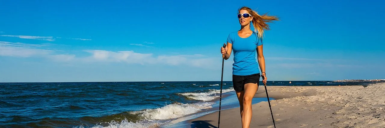 Eine Frau in einem kurzen Oberteil macht Nordic-Walking am Strand.
