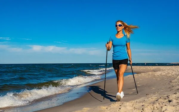 Eine Frau in einem kurzen Oberteil macht Nordic-Walking am Strand.