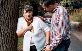 Eine ältere Frau mit Herzinsuffizienz muss eine Pause auf ihrem Spaziergang machen. Ein Mann hilft ihr.