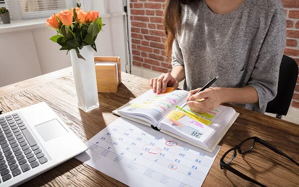 Eine Frau sitzt am Tisch und macht sich Notizen in ihrem Kalender.