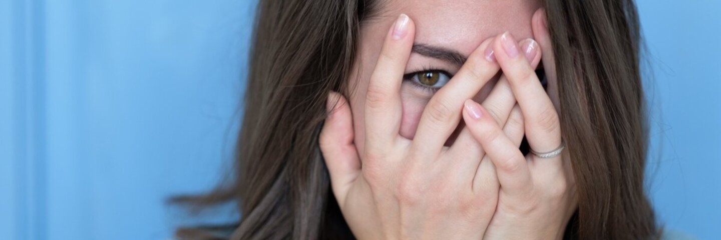 Brünette Frau schämt sich und hält ihre Hände vor das errötete Gesicht