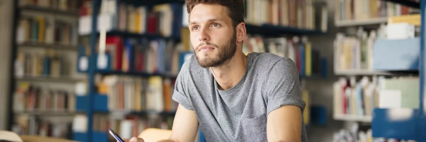 Student sitzt in Bibliothek und denkt nach, ob er wirklich so schlau ist.