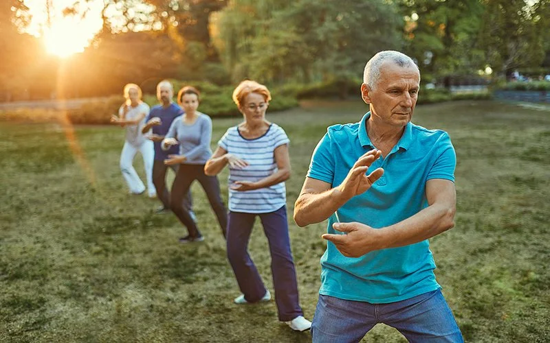 Fünf Menschen machen in einem Park gemeinsam Tai-Chi-Übungen.