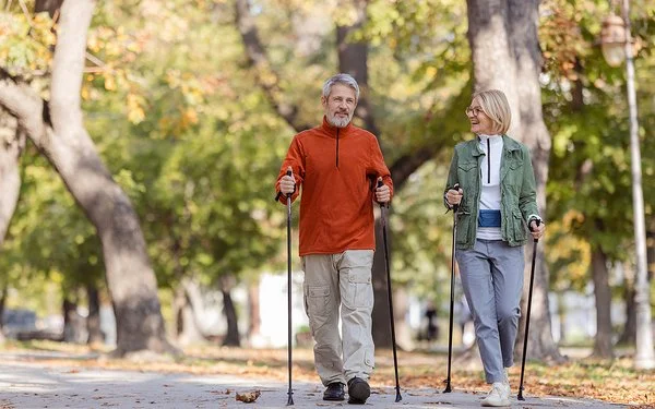 Ein Mann und eine Frau in sportlicher Freizeitkleidung beim Nordic-Walking in einem herbstlichen Park.