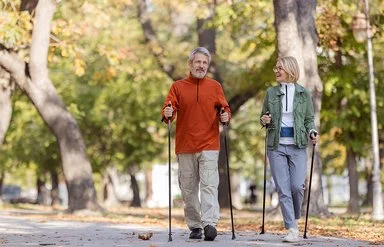Ein Mann und eine Frau in sportlicher Freizeitkleidung beim Nordic-Walking in einem herbstlichen Park.