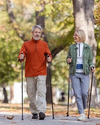 Ein Mann und eine Frau in sportlicher Freizeitkleidung beim Nordic-Walking in einem herbstlichen Park.