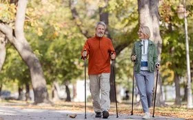 Ein Mann und eine Frau in sportlicher Freizeitkleidung beim Nordic-Walking in einem herbstlichen Park.