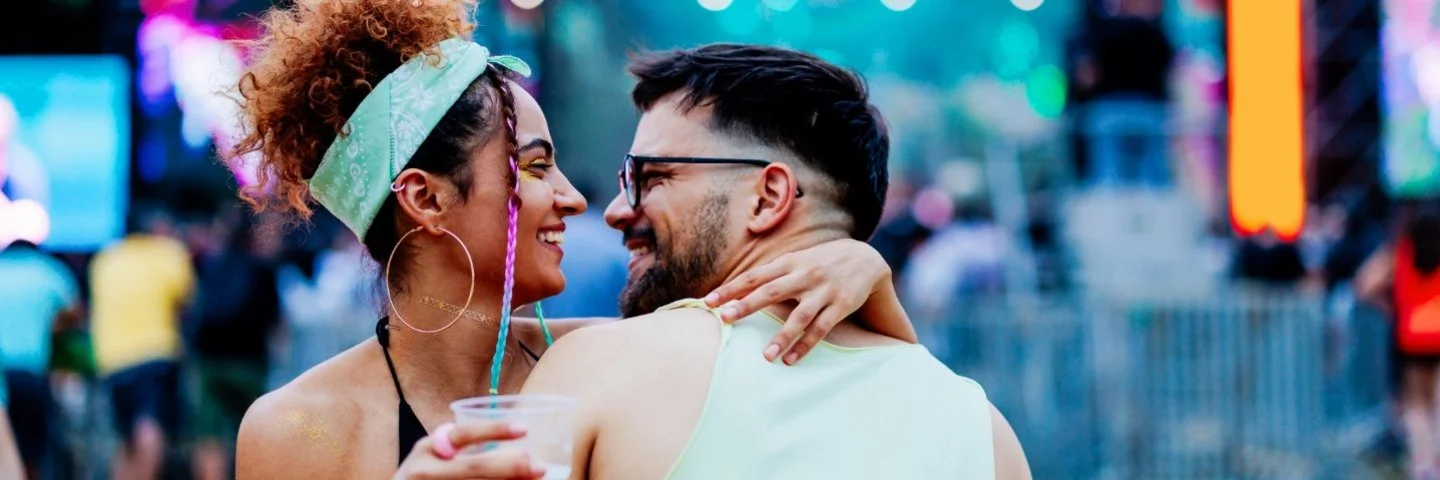 Ein glückliches Paar umarmt sich vor einer Musikbühne stehend und inmitten einer Menschenmenge.