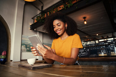 Eine junge Frau sitzt in einem Café und liest auf ihrem Tablet-Computer. Mit den News der AOK ist sie immer gut informiert.