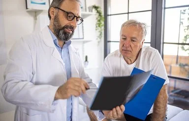 Ein Arzt und ein älterer Patient schauen sich gemeinsam Dokumente an.