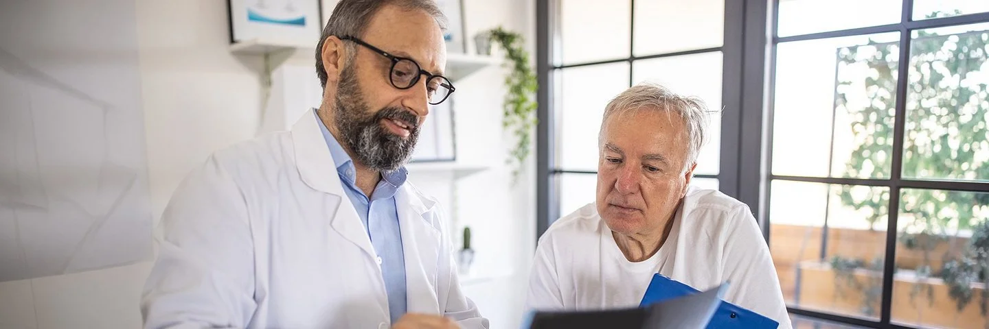 Ein Arzt und ein älterer Patient schauen sich gemeinsam Dokumente an.