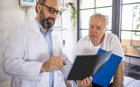 Ein Arzt und ein älterer Patient schauen sich gemeinsam Dokumente an.