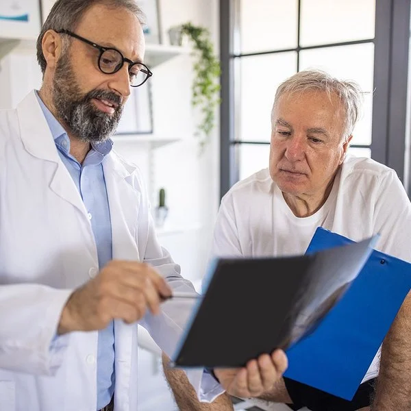 Ein Arzt und ein älterer Patient schauen sich gemeinsam Dokumente an.