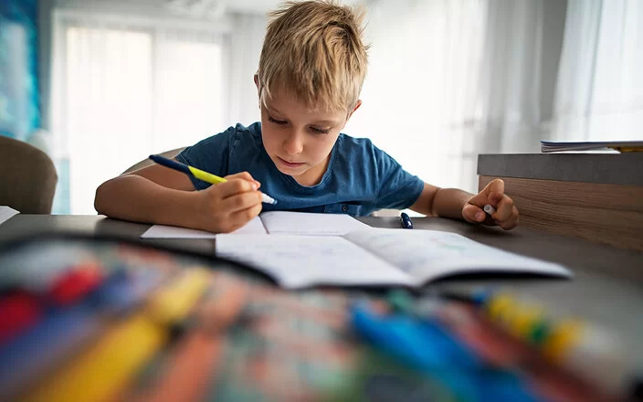 Ein etwa siebenjähriger Junge sitzt an seinem Schreibtisch und macht Hausaufgaben.