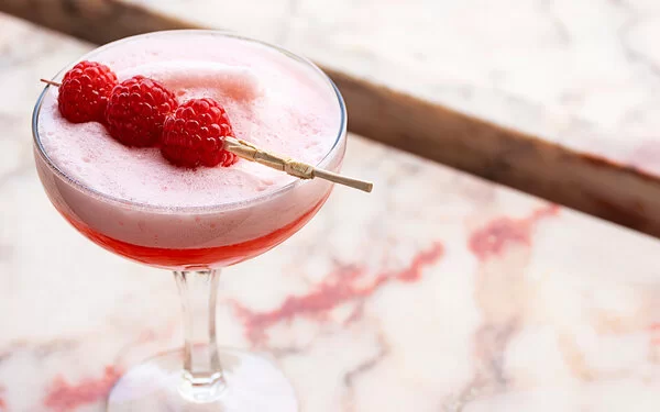 Alkoholfreier Clover Club in einem Cocktailglas auf einer Marmorplatte, garniert mit frischen Himbeeren.