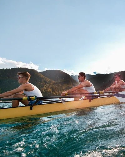 Vier Männer in sportlicher Kleidung rudern in einem Ruderboot auf einem See.