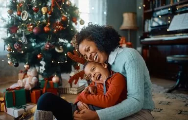 Eine Mutter umarmt ihr lachendes Kind vor einem Weihnachtsbaum