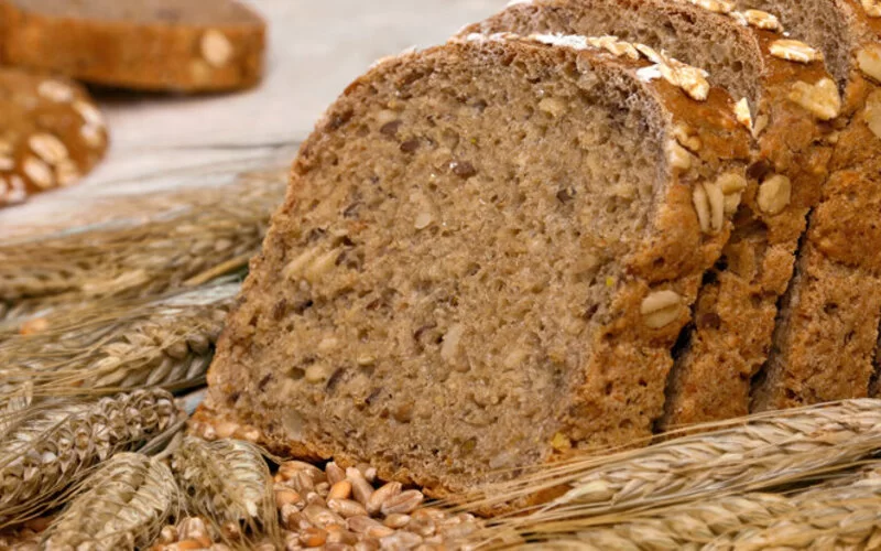 Ein Laib Vollkornbrot aufgeschnitten und Gerstenspelzen auf einem Tisch drapiert.