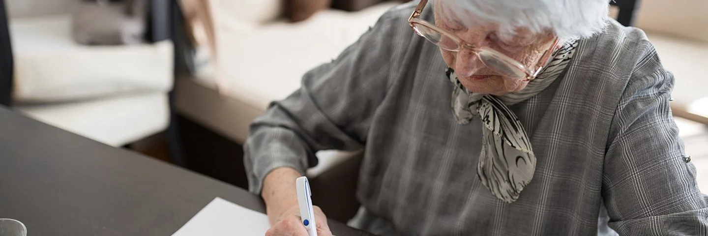 Seniorin sitzt an einem Tisch und macht einen Demenztest.