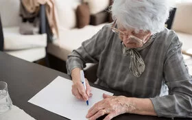 Seniorin sitzt an einem Tisch und macht einen Demenztest.