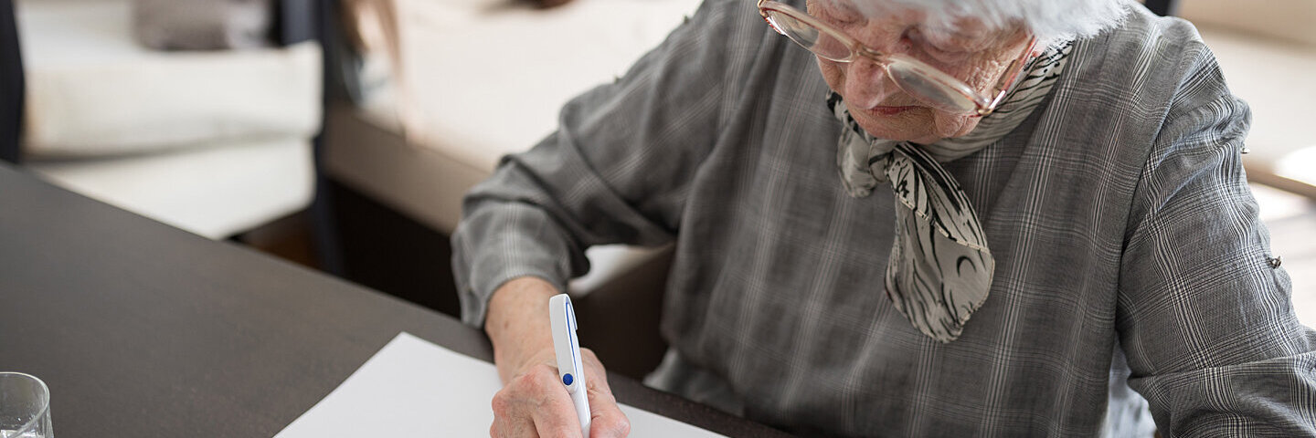 Seniorin sitzt an einem Tisch und macht einen Demenztest.