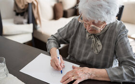 Seniorin sitzt an einem Tisch und macht einen Demenztest.