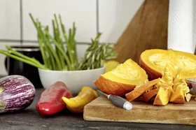 Das Bild zeigt ein Holzbrett, das in der Küche steht. Auf dem Brett liegt Obst und Gemüse.