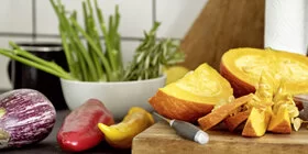 Das Bild zeigt ein Holzbrett, das in der Küche steht. Auf dem Brett liegt Obst und Gemüse.