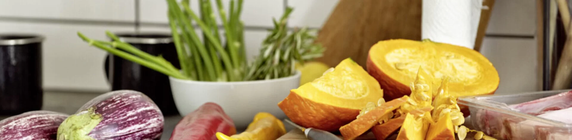 Das Bild zeigt ein Holzbrett, das in der Küche steht. Auf dem Brett liegt Obst und Gemüse.