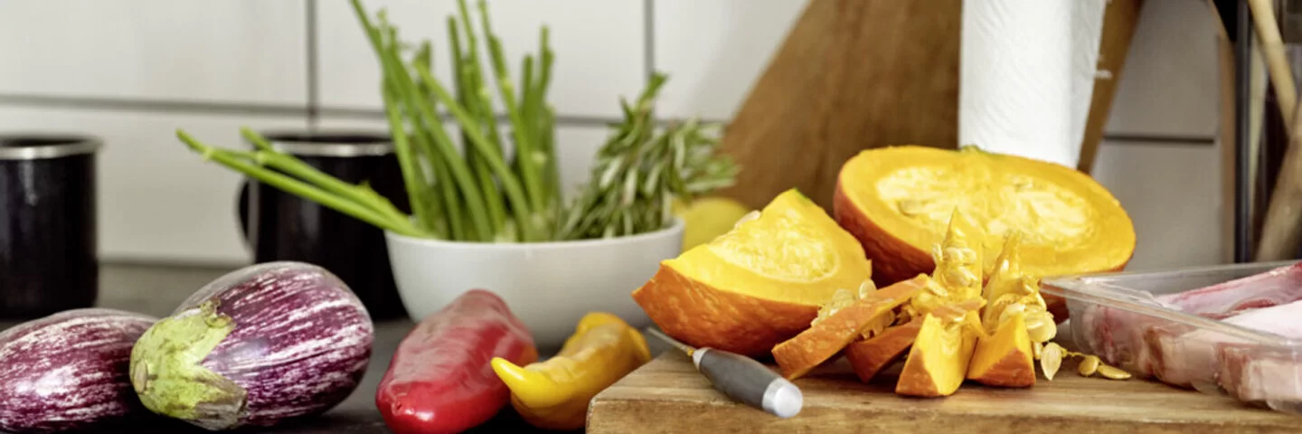 Das Bild zeigt ein Holzbrett, das in der Küche steht. Auf dem Brett liegt Obst und Gemüse.