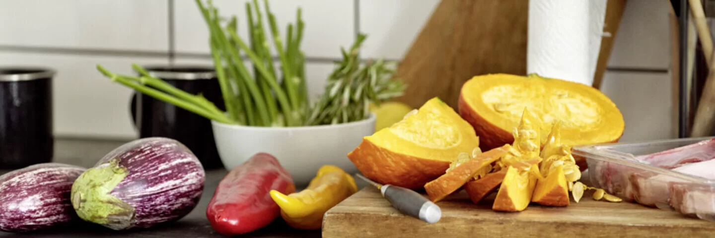 Das Bild zeigt ein Holzbrett, das in der Küche steht. Auf dem Brett liegt Obst und Gemüse.