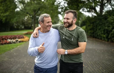 Ein junger und ein älterer Mann treiben in einem Park sport und lachen gemeinsam.
