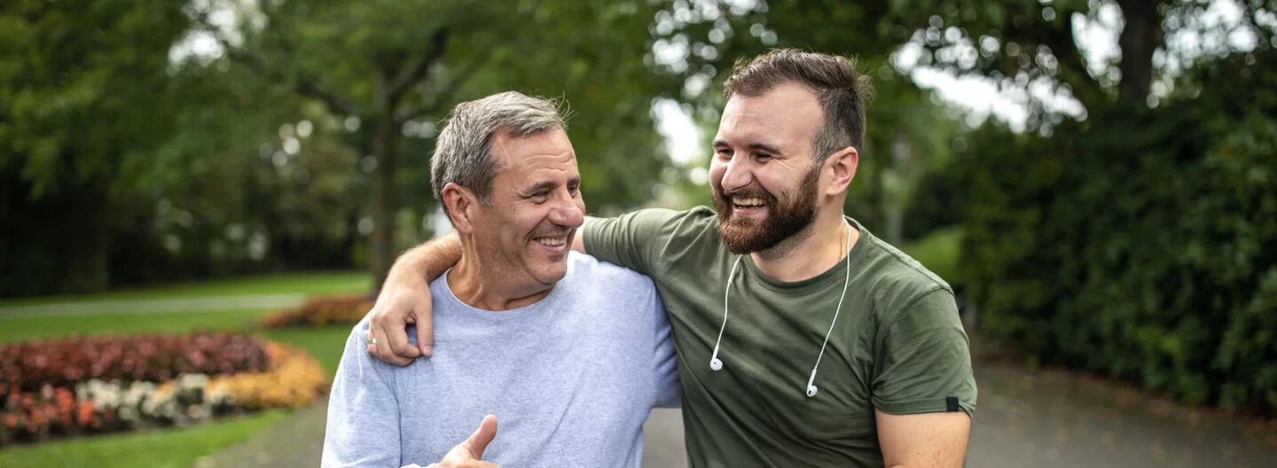 Ein junger und ein älterer Mann treiben in einem Park sport und lachen gemeinsam.
