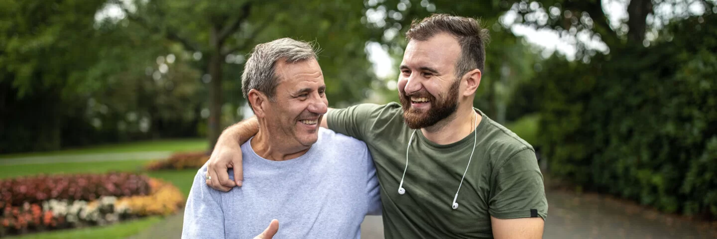 Ein junger und ein älterer Mann treiben in einem Park sport und lachen gemeinsam.