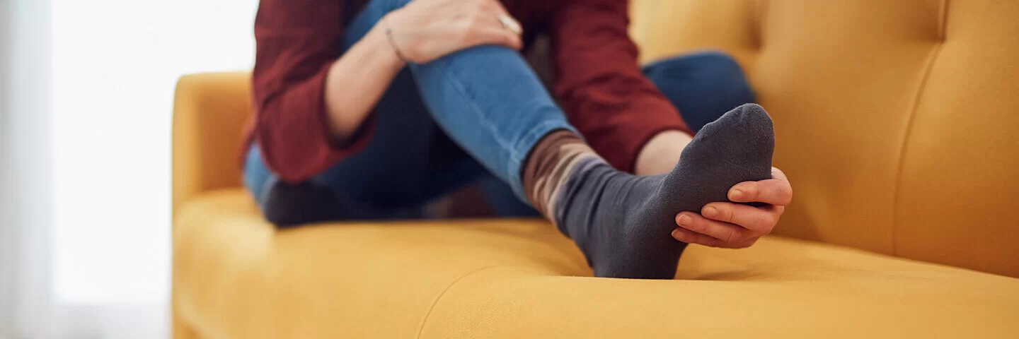 Frau sitzt auf dem Sofa und massiert ihren schmerzenden Spreizfuß.