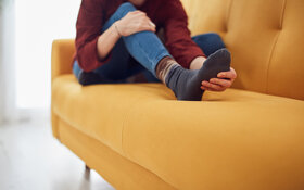 Frau sitzt auf dem Sofa und massiert ihren schmerzenden Spreizfuß.