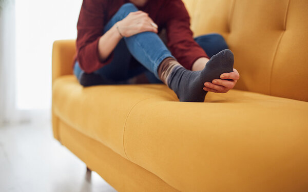 Frau sitzt auf dem Sofa und massiert ihren schmerzenden Spreizfuß.