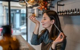 Eine junge Frau hält in der linken Hand eine Pipette. Ihr rechtes Handgelenk hat sie an der Nase. Es wirkt, als ob der Geruch angenehm ist.