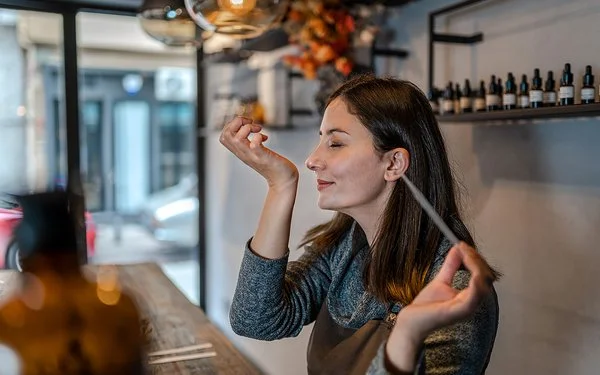 Eine junge Frau hält in der linken Hand eine Pipette. Ihr rechtes Handgelenk hat sie an der Nase. Es wirkt, als ob der Geruch angenehm ist.