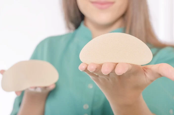 Eine junge Frau hält Brustprothesen in ihren Händen.