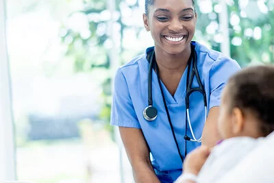 Eine Frau in blauer Arbeitskleidung lächelt ein Mädchen an, das in einem Krankenhausbett liegt.