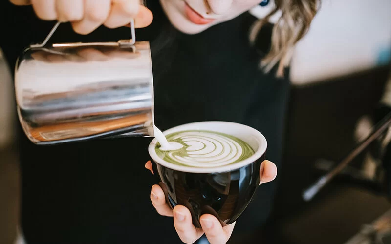 Eine Barista bereitet einen Matcha-Latte mit Latte Art zu.