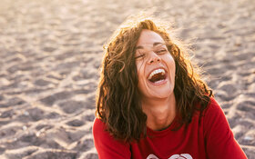 Eine Frau am Strand lacht herzhaft im Sonnenuntergang.