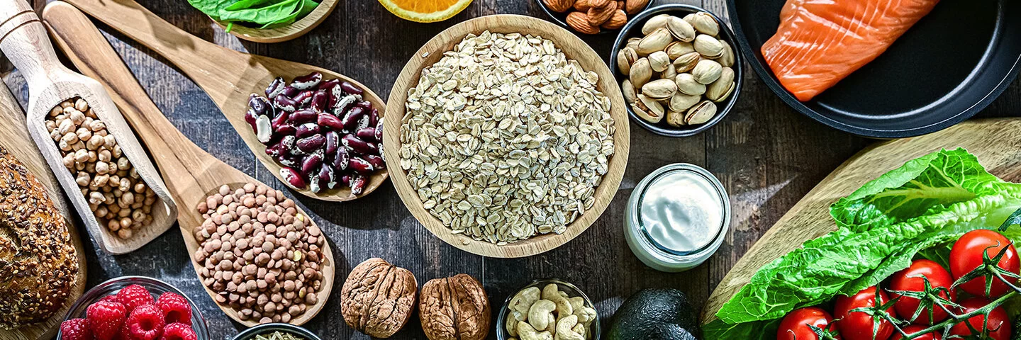 Auf einem Tisch sind Hülsenfrüchte, Salat, Gemüse, Obst, Lachs und Vollkornbrot angerichtet.