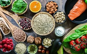 Auf einem Tisch sind Hülsenfrüchte, Salat, Gemüse, Obst, Lachs und Vollkornbrot angerichtet.