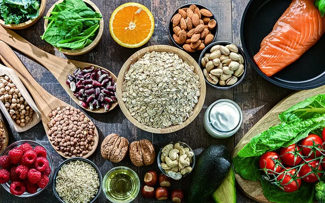 Auf einem Tisch sind Hülsenfrüchte, Salat, Gemüse, Obst, Lachs und Vollkornbrot angerichtet.