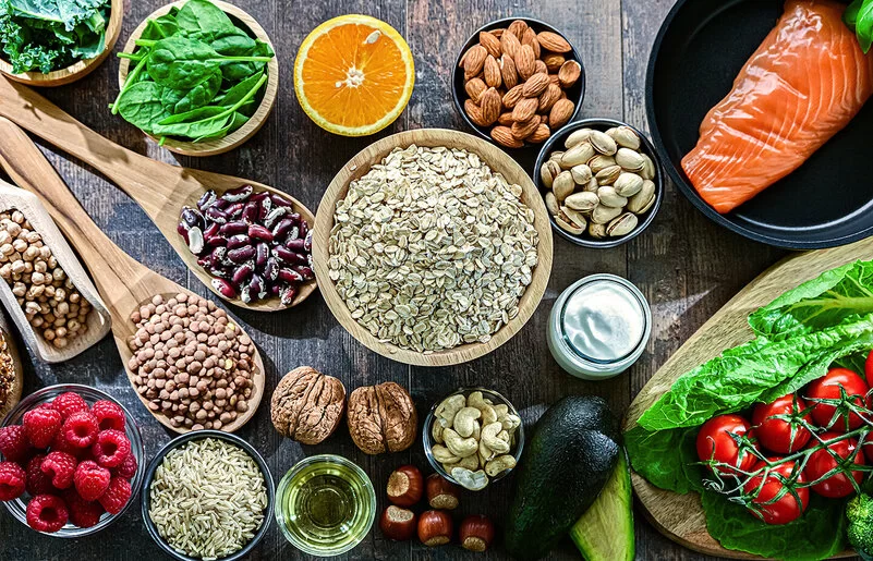 Auf einem Tisch sind Hülsenfrüchte, Salat, Gemüse, Obst, Lachs und Vollkornbrot angerichtet.