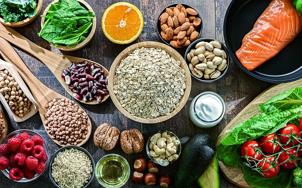 Auf einem Tisch sind Hülsenfrüchte, Salat, Gemüse, Obst, Lachs und Vollkornbrot angerichtet.